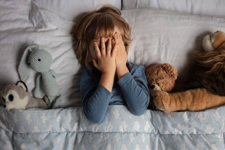Un enfant fait des cauchemars dans son lit entouré par des peluches